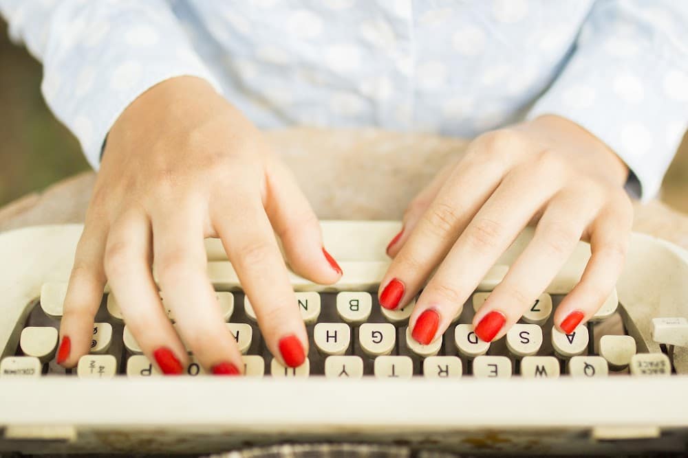 woman with red nails typing on a typewriter
