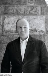 portrait of Michael Ledwidge in black and white wearing a jacked and open neck shirt