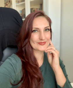 Photo of the author Madeleine Martin a woman sitting ina chair with brownish red hair and red lipstick