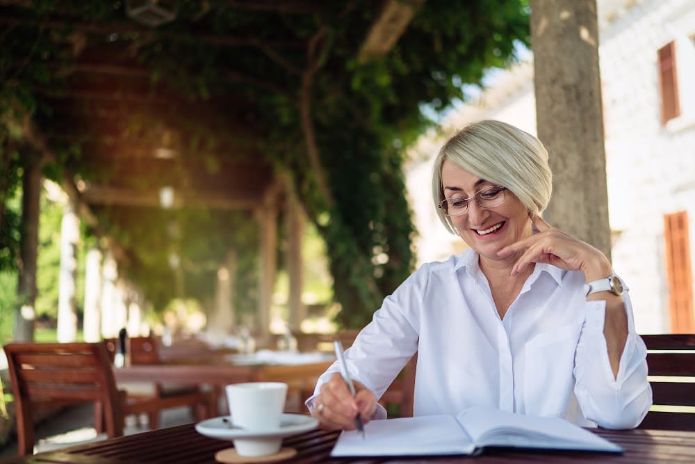 woman over 40 sitting outside writing a novel with a cup of coffee