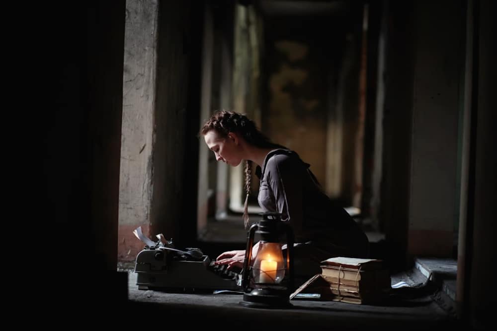 woman sitting at a typewriter in a gothic window with a lantern