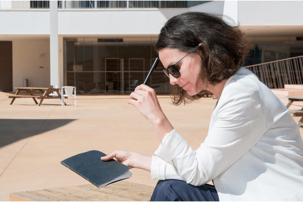 woman over 40 sitting outside with a pen and notebook thinkin about writing a first draft